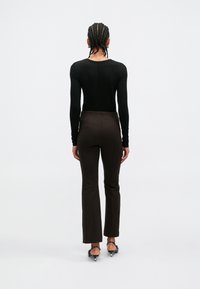 Haut noir à manches longues associé à un pantalon marron taille haute et fuselé. Présente une texture lisse et une silhouette ajustée. Chaussures noires à talons.