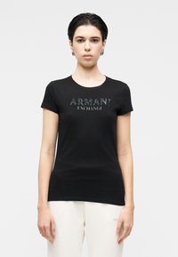 Melnā kokvilnas t-krekls ar īsām piedurknēm, krūškurvja daļā ar spīdīgu "ARMANI EXCHANGE" logo. Vienkāršs, pieguļošs dizains.