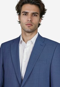 Junger Mann mit schulterlangen Haaren, der ein blaues Sakko über einem weißen Hemd trägt und mit neutralem Ausdruck direkt in die Kamera schaut.