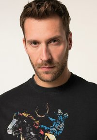 Schwarzer Sweatshirt mit einem bunten Grafikdesign eines Cowboys auf einem Pferd. Das Design hat eine vintage Textur, einen Rundhalsausschnitt und gerippte Bündchen.