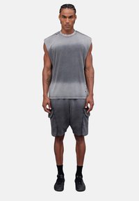 Top grigio senza maniche e pantaloni abbinati, caratterizzati da un effetto sfumato sbiadito. Tessuto morbido, vestibilità ampia, con cuciture visibili e tasche. Sneakers nere.