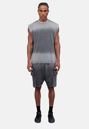 Top sin mangas gris y pantalones cortos a juego, con un efecto de degradado desvanecido. Tela suave, corte holgado, con costuras visibles y bolsillos. Zapatillas negras.