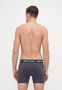Grau Boxershorts mit einem schwarzen elastischen Bündchen, das mit weißer "ellesse"-Markierung versehen ist. Glatte Textur und enganliegendes Design, von hinten betrachtet.