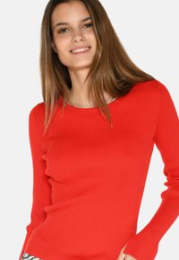 Rotes, geripptes Langarmoberteil mit rundem Halsausschnitt. Es zeichnet sich durch ein körpernahes Design und eine weiche Textur aus, die eine glatte und stabile Silhouette zur Schau stellt.