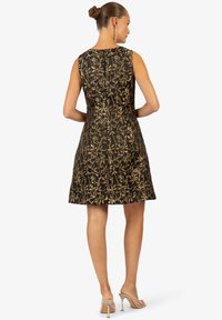 Robe noire avec motif de feuilles dorées, design sans manches, longueur genou, texture lisse, dotée d'une fermeture éclair dissimulée à l'arrière.