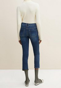 Mörkblå avkortade jeans med hög midja, femficksdesign, synlig söm och slim fit, i kombination med en ljus långärmad topp.