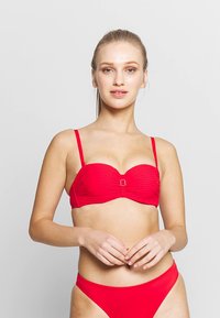 Raudonas bikinis su klostuotu dizainu, reguliuojamomis petnešėlėmis ir mažu metaliniu akcentu priekyje. Lygus paviršius ir klasikinis kirpimas.