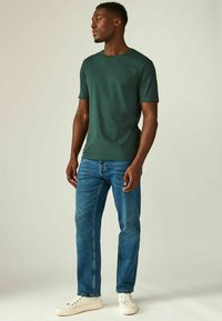Grøn kortærmet t-shirt med rund hals, parret med blå denim jeans og hvide sneakers. Glat stof, tætsiddende design, standard snit.