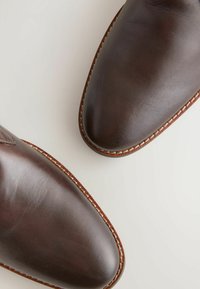 Ciemnobrązowe skórzane buty z wysmukłymi czubkami, widocznym przeszyciem wzdłuż podeszw i gładką teksturą. Dwie pary pokazane z góry.