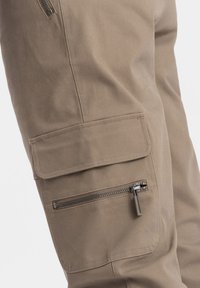 Pantaloni cargo beige con tasca a pattina laterale e tasca con zip in metallo, realizzati in un tessuto resistente con una superficie liscia.
