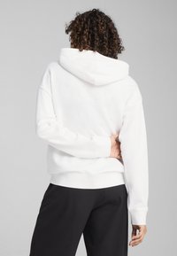 Felpa bianca con cappuccio, dotata di polsini e bordo a costine, caratterizzata da una vestibilità rilassata. Il tessuto appare liscio con una consistenza leggera.