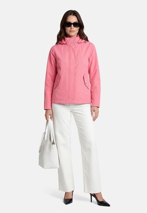 Woman wearing black sunglasses, pink hooded jacket, white wide-leg pants, black heels, holding a white handbag, standing against a plain background.