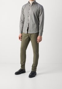 Šedá košile na knoflíky s malými modrými tečkami, kombinovaná s olivově zelenými slim-fit kalhotami a černými botami se zlatými kovovými detaily.