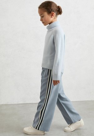 Vaaleansininen pooloneule, jossa on resorireuna, yhdistettynä leveisiin vaaleansinisiin housuihin, joissa on pystysuoria raitoja, sekä valkoisiin tennareihin.