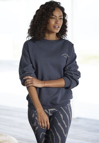 Felpa blu navy con polsini e orlo a coste, arricchita con testo ricamato bianco. Abbinata a leggings a fantasia in tonalità scure e chiare.