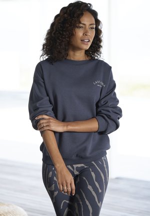 Marineblauwe sweatshirt met ribgebreide mouwen en onderkant, met witte geborduurde tekst. Gecombineerd met gestreepte leggings in donkere en lichte tinten.