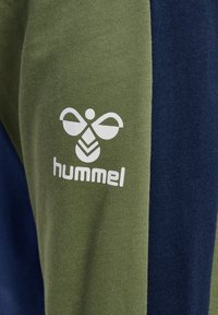 Groene en marineblauwe katoenen stofmix met een textuurfinish. Bevat een wit logo op het groene gedeelte, met contrasterende kleuren aan de zijkanten.