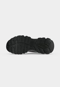 Semelle noire de sneaker avec des rainures profondes et un motif de bande de roulement texturé conçu pour l’adhérence et la durabilité sur une surface plane.