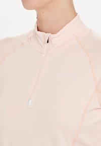 Helles rosa Sportoberteil mit Viertelreißverschluss, aus weichem Stoff gefertigt, mit kontrastierenden Nähten und einem kleinen Logo auf der Brust.