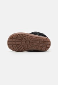 Chaussures noires avec une surface douce et texturée et une semelle en caoutchouc dotée d'un motif antidérapant. La semelle est de couleur marron clair.