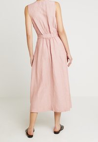 Rosa linne maxikjol med ärmlös design, elastisk midja och flödande kjol. Har en mjuk textur och en enkel silhuett.