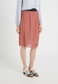 Plisseret midi-nederdel i rustfarve med elastisk sort linning, kombineret med flerfarvede sandaler med blokhæl.