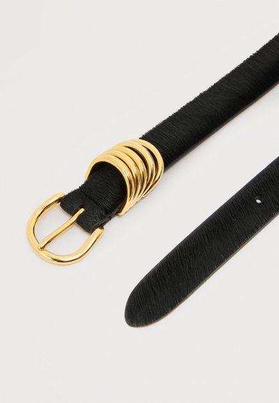 Μαύρη υφασμάτινη ζώνη με χρυσή πόρπη και πέντε χρυσούς κρίκους, απλωμένη σε λευκή επιφάνεια.