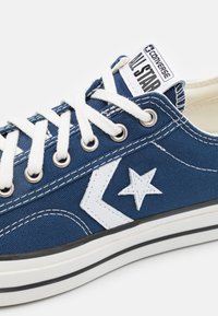 Blue canvas sneaker with white accents, featuring metal eyelets, white laces, and a rubber sole. Prominent star logo on the side.