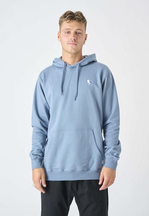 Helle blaue Kapuzenjacke aus weichem Material, mit einer Fronttasche und einem kleinen Vogelmotiv auf der linken Brust. Lange Ärmel mit gerippten Bündchen.