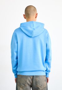 Haut à capuche bleu clair avec un cordon de serrage et des poignets côtelés, fabriqué en coton doux, avec une texture lisse et une coupe décontractée.