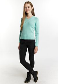 Menta zöld V-nyakú pulóver, bordás aljjal, fekete skinny farmernadrággal és fekete fűzős csizmával párosítva. SIMA kötött textúra, slim fit.