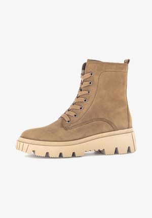 Bottines en suede beige avec lacets, dotées d'une semelle épaisse beige et d'un relief texturé. Elles présentent un design montante et six œillets pour les lacets.