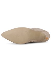 Tacón de ante beige con un upper suave y una suela de goma texturizada. Presenta una puntera afilada y un pequeño acento naranja en el tacón.
