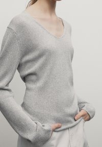 Light gray long-sleeve sweater with a V-neck, made of a textured knit fabric. Loose fit, with cuffs extending slightly over hands.