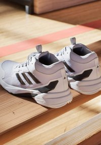 Białe buty sportowe z czarnymi akcentami, z teksturowaną cholewką, wyściełanym kołnierzem i charakterystycznym trzy-paskowym wzorem po bokach.