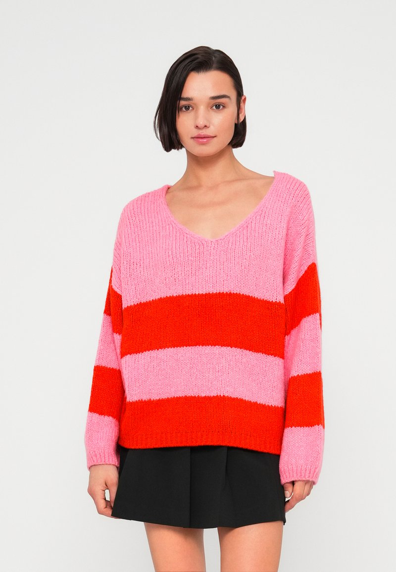 Pull tricoté à col en V, présentant des rayures horizontales rose et rouge. Manches longues, coupe décontractée et finition texturée.