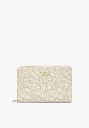 Billetera beige con un patrón texturizado y ondulado, con letras en tono dorado "TOUS". Cierre de cremallera y material de tela. Forma rectangular compacta.