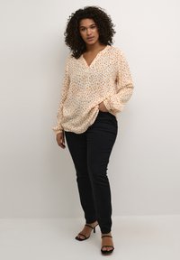 Loose-fitting, long-sleeve shirt in light peach with a spotted pattern in orange and blue. Paired with black slim-fit pants and black strappy heels.