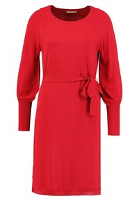Robe tricotée rouge avec un col rond, de longues manches ballon et une ceinture nouée à la taille. Texture lisse et longueur au genou.
