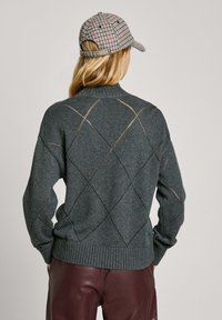 Dark grey knitted sweater with diamond patterns and open stitches. Features a high neckline and ribbed hem. Worn with burgundy leather pants.