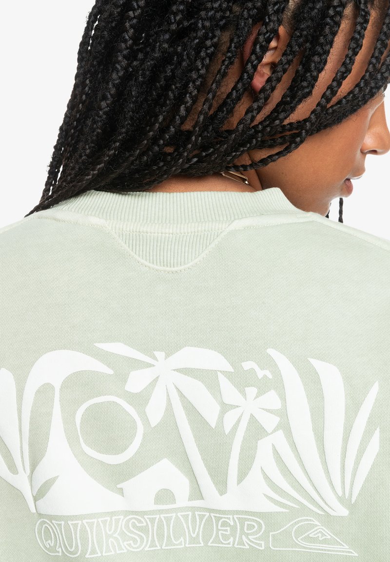 Helles grünes Sweatshirt mit strukturiertem Finish, das auf der Rückseite ein weißes tropisches Grafikdesign mit Palmen und Formen zeigt.