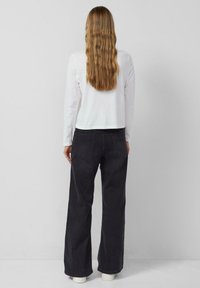 Biały, długi rękaw, krótki top w połączeniu z czarnymi, wysokim stanem, szerokimi spodniami dżinsowymi, z tylnymi kieszeniami i teksturowanym materiałem.