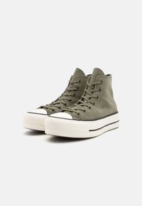 Zapatillas altas en ante verde oliva, con puntera de goma blanca y suela plataforma con rayas negras, y diseño de cierre con cordones.