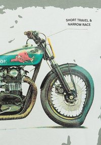 Motocicleta con un chasis en color turquesa, motor cromado y rueda de radios. Muestra un gráfico rojo en el tanque, que presenta un texto sobre la suspensión.