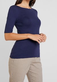 Marinblåt figurnära T-shirt med båthals och ärmar som går till armbågen, tillverkad av ett mjukt tyg, i kombination med rutiga bruna byxor.