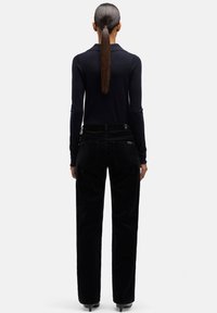 Czarne spodnie sztruksowe o prostych nogawkach, zestawione z dopasowaną granatową bluzką z długim rękawem, widok od tyłu, podkreślający czyste linie.