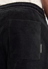 Nahaufnahme einer schwarzen Cordhose mit Gesäßtasche, elastischem Bund und Marc O'Polo-Label an der Seite.