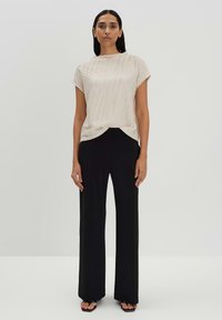 Top testurizzato beige chiaro con maniche corte abbinato a pantaloni neri a vita alta e sandali neri con punta aperta.