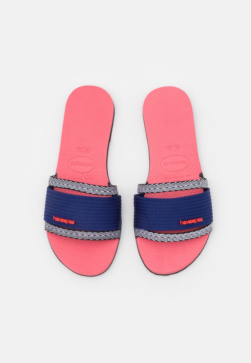 Chaussons à semelle texturée rose en bleu marine, avec des sangles élastiques et un motif en chevron, marqués du logo "havaianas" en rouge.