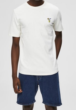 Weißes Kurzarm-T-Shirt aus Baumwolle, mit einem kleinen gestickten Design eines Getränks mit einer Zitrone und einem Strohhalm auf der linken Brustseite.